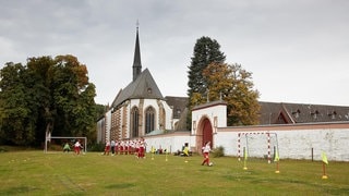 Ein Kloster mit einem Fußballplatz. Dort trainiert eine junge Jungenmannschaft. Szenenbild aus dem Hamburger Tatort „Schweigen“ mit Kommissar Falke.