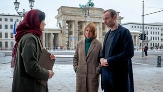 Tatort-Duo Susanne Bonard und Robert Karow sprechen mit einer Frau vor dem Brandenburger Tor in Berlin